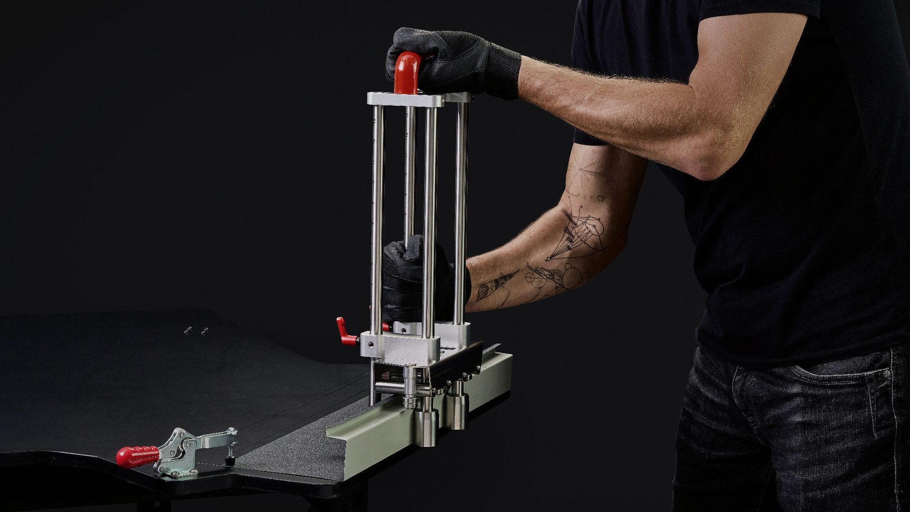 Gloved hands adjusting an upright metal seaming tool on a small steel table against black.